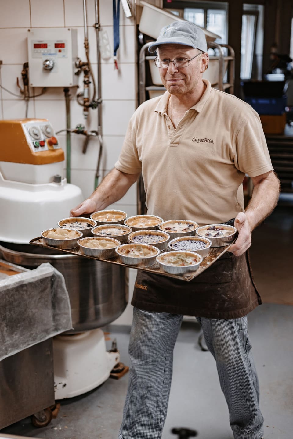 Bäcker trägt ein Blech mit Quiches durch die Backstube