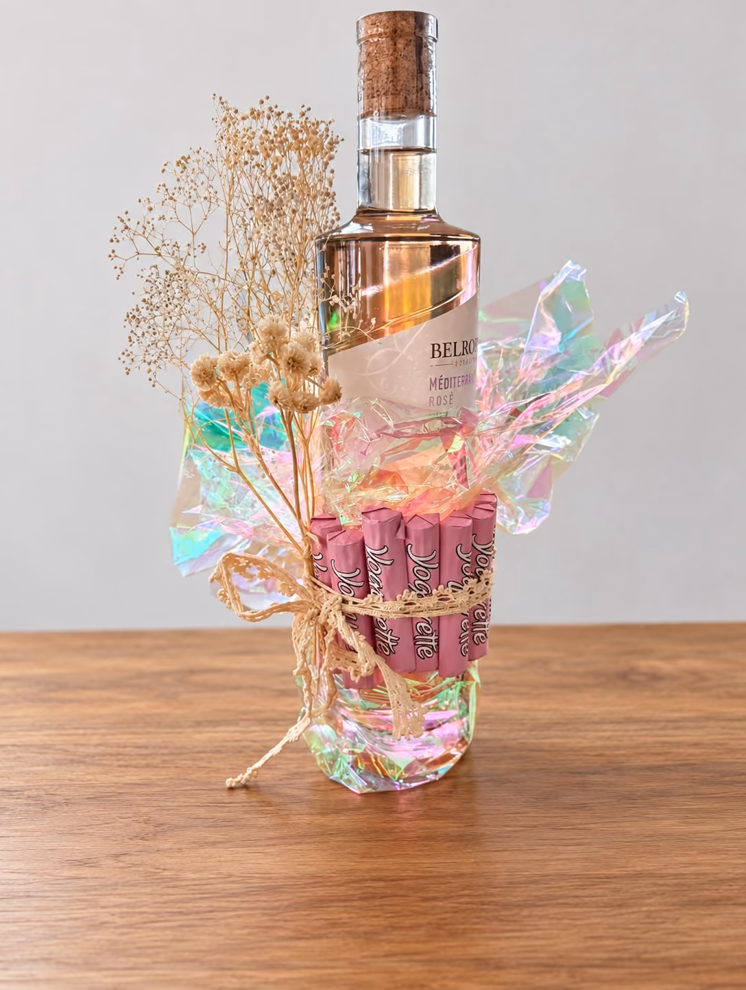 Flasche Rosé, verziert mit Schillerfolie, rosa Süssigkeiten, Spitzenband und Trockenblumen